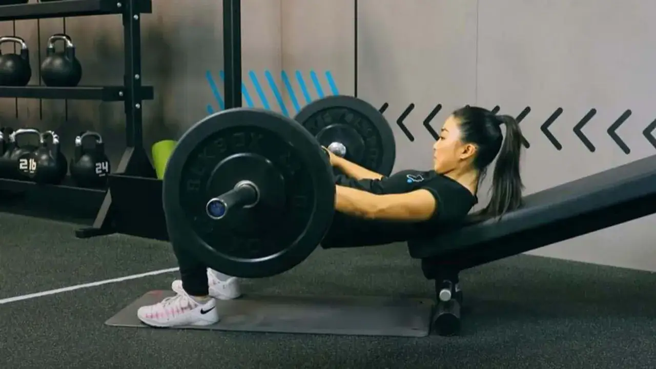 Donna esegue un hip thrust con bilanciere su una panca inclinata, concentrata sull'allenamento.